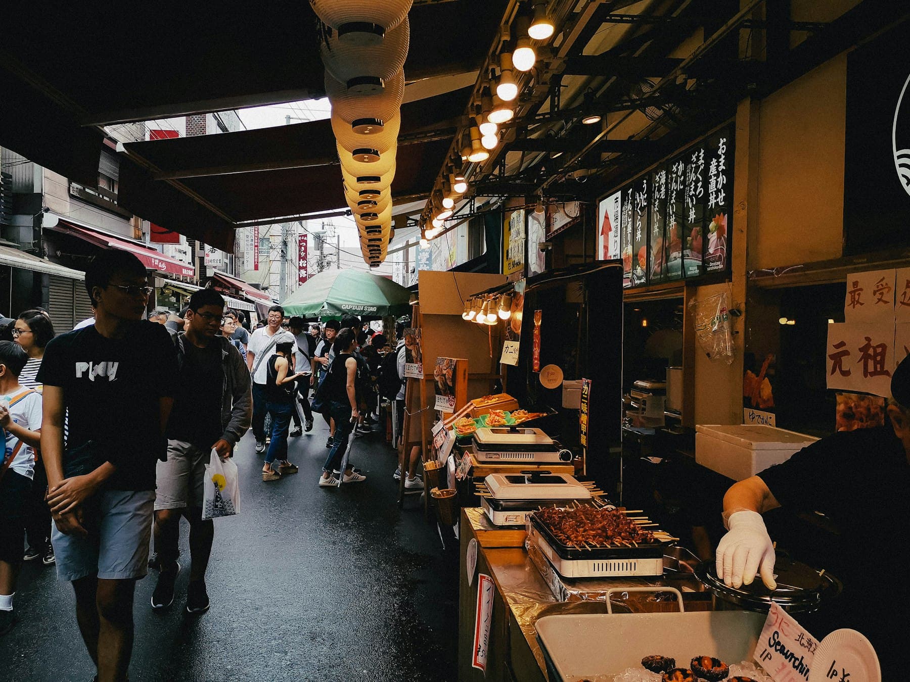 En livlig matgata vid Tsukiji i Tokyo med matstånd och besökare